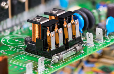 Electronic components as electromagnetic relays or glass electric fuse on green PCB. Closeup two...
