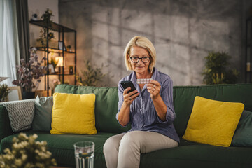 Mature woman hold the medicine and read instructions on mobile phone