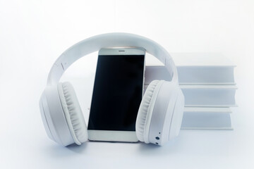 Audio books concept. Modern Tech Setup. White headphones around a smartphone, with a stack of books