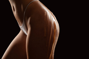 Beautiful sexy ass of young naked woman on black background. Drops of honey flow down on her...