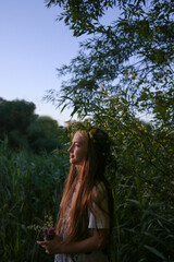 9 years old girl standing in a wreath of wildflowers on the shore of a pond