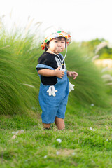 Little Caucasian girl, 1 year old, wearing casual clothes, running on the green grass in the park, spending time outdoors in the village,A young girl learning to walk in a hat walks happily in the par