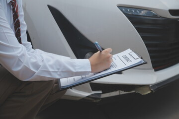Side view of writing on clipboard while insurance agent examining car after accident