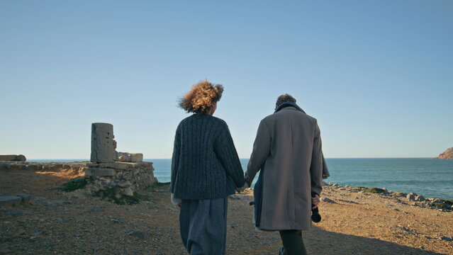 Romantic pair walking ocean beach back view. Diverse couple in love strolling
