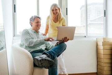 Smiling mature couple using laptop in bright room