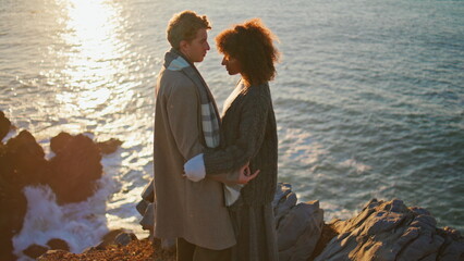 Fototapeta premium Diverse spouses bonding evening standing on sunny seacoast. Lovers embracing