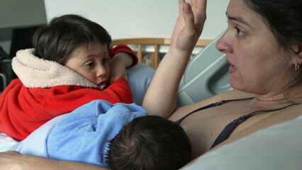 Fototapeta premium Mother breastfeeding newborn while older child leans on her, conveying the warmth and closeness of family life and the support that older siblings provide during early parenting