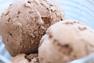 A close-up shot of three scoops of chocolate ice cream in a glass bowl