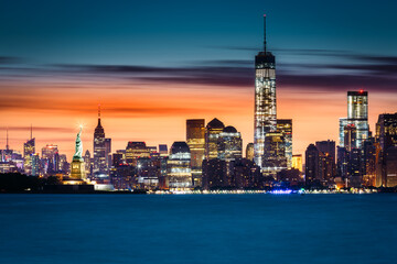 Obraz premium Sunrise over New York City with the Statue of Liberty illuminated in front of the Manhattan skyline.