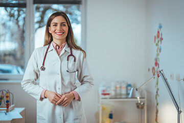 A joyful Caucasian woman in medical professional attire stands confidently with hands clasped,...