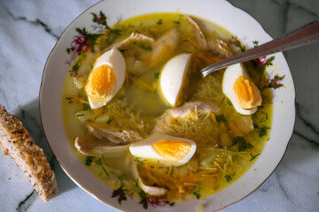 Homemade chicken soup with eggs and noodles and a slice of bread, top view
