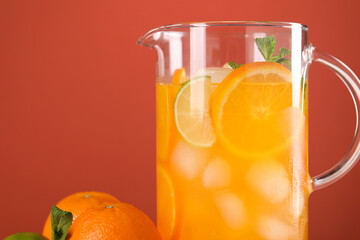 Freshly made lemonade in jug and citrus fruits against coral background