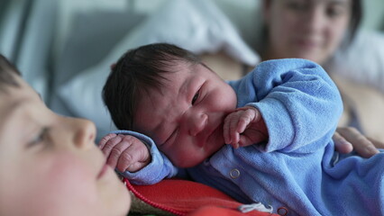 Newborn baby wearing blue onesie, peacefully resting on older sibling's chest, with a tender sibling bond, capturing the warmth and love in a family setting