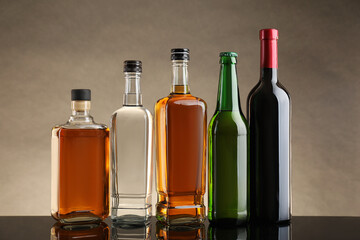 Bottles with different alcoholic drinks on table against beige background