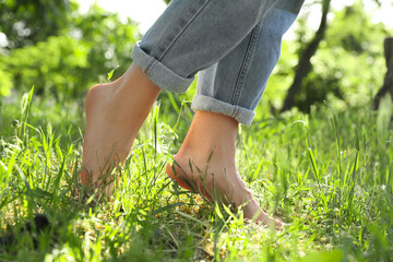 Woman walking barefoot on green grass outdoors, closeup