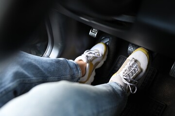 Woman in sneakers pushing on pedal of car brake, closeup