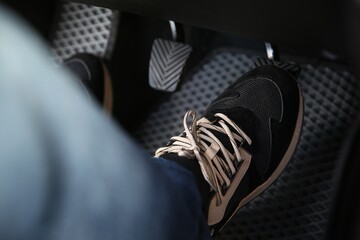 Man in sneakers pushing on pedal of car brake, closeup