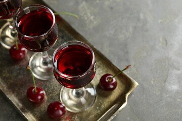 Delicious cherry liqueur in glasses and fresh berries on grey table, space for text