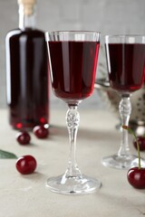 Delicious cherry liqueur in glasses, fresh berries and bottle on light grey table