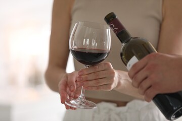 Man pouring red wine into woman`s glass indoors, closeup