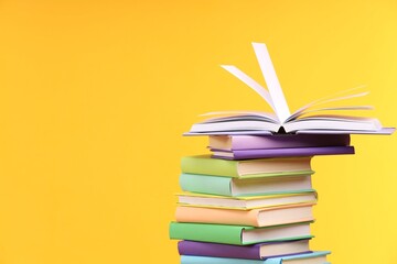 Stack of colorful books on yellow background, space for text