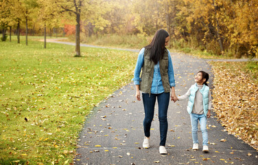 Mom, walking and holding hands with little girl for bonding, outdoor adventure or journey in nature. Mother strolling with child, kid or daughter on sidewalk or path in autumn season at park outside