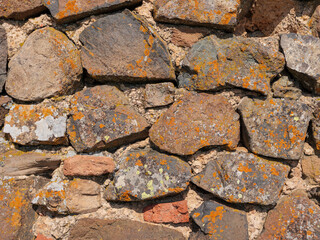 A close-up texture shot of an ancient stone wall. The stones are weathered and show signs of age, with lichen growing on their surface.