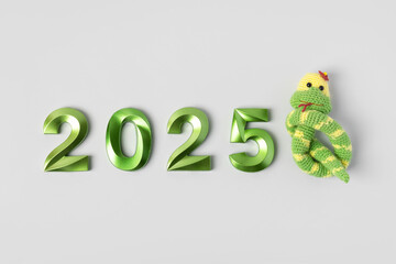 Knitted toy striped green snake and green numbers. The symbol of the year 2025 on a gray background.