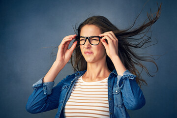 Surprise, woman and glasses with wind in studio for hair blow, crazy weather and comedy for good news as winner. Shocked, female geek with eyewear for lottery giveaway, wow and blue background