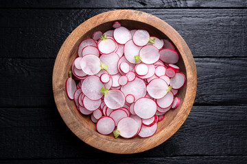 Thin radish slices in a wooden plate on black rustic table. Vegetable salad. Food photography