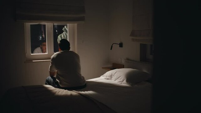 Silhouette sad man sitting bed home looking window feeling lonely. Guy insomnia
