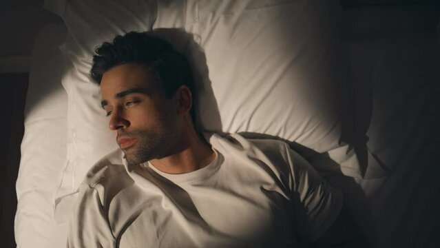 Man lying night bed suffering from insomnia closeup top view. Sad guy on pillow