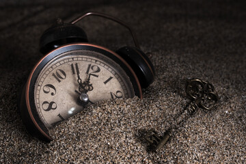 Alarm clock buried in sand. Time is money concept.
