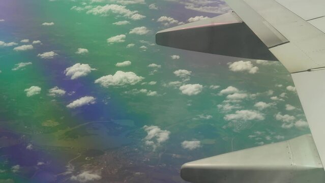 Porthole view of an airplane wing and eath clouds during northern lights or magnetic storm with a rainbow in the clouds. Airliner maneuver in the sky