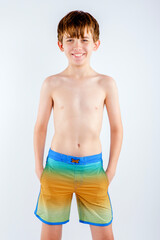 Smiling young teen beach boy standing with his hands in the pockets of his colorful swim trunks
