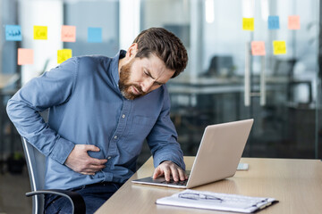 Businessman experiencing stomach pain at office while working on laptop