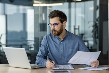 Serious financier working on paperwork and analyzing data in modern office