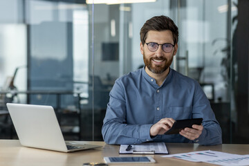 Portrait of businessman using tablet and laptop in modern office