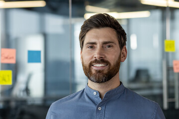 Naklejka premium Confident businessman with beard smiling in office setting with glass walls and sticky notes