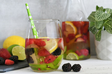 Water infused with berries and citrus slices or summer berry sangria - drink in glass with carafe in background
