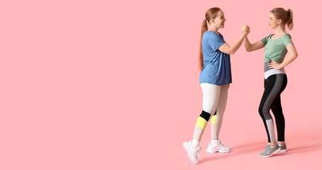 Obraz premium Portrait of sporty young women holding hands on pink background with space for text