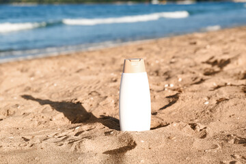 Bottle of sunscreen cream on sand near ocean at beach