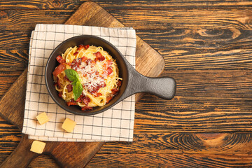 Frying pan with tasty pasta carbonara on wooden background