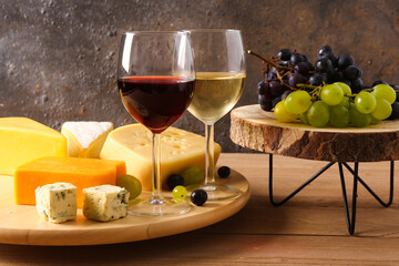 Wooden board with tasty cheese, grapes and glasses of wine on table