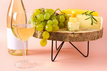 Wooden stand with tasty cheese, grapes, bottle and glass of wine on pink background