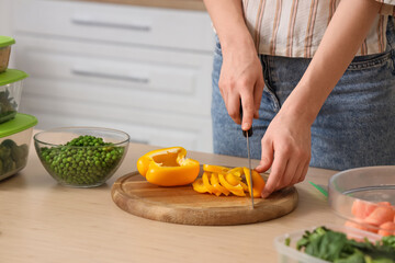 Woman cutting bell pepper for freezing in kitchen