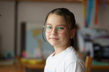 A small beautiful teenage girl in glasses with a hairstyle sitting at the piano. Blurred children's room in the background. Childhood education concept