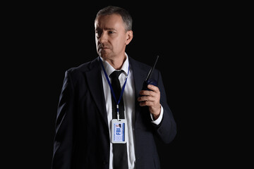 Mature FBI agent with two-way radio on black background