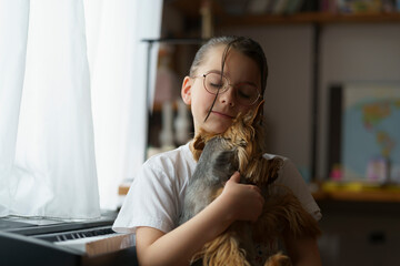 A small beautiful teenage girl in glasses with a hairstyle sitting at the piano with a dog. Blurred children's room in the background. Concept of education, childhood and friendship with a pet