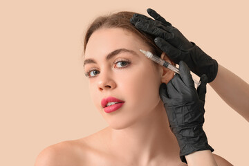 Young woman receiving filler injection in forehead on beige background